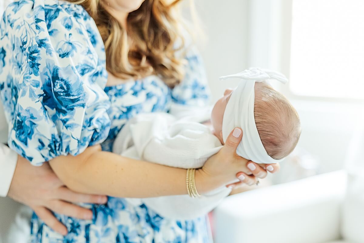 mom holding swaddled newborn baby birl in blue floral dress